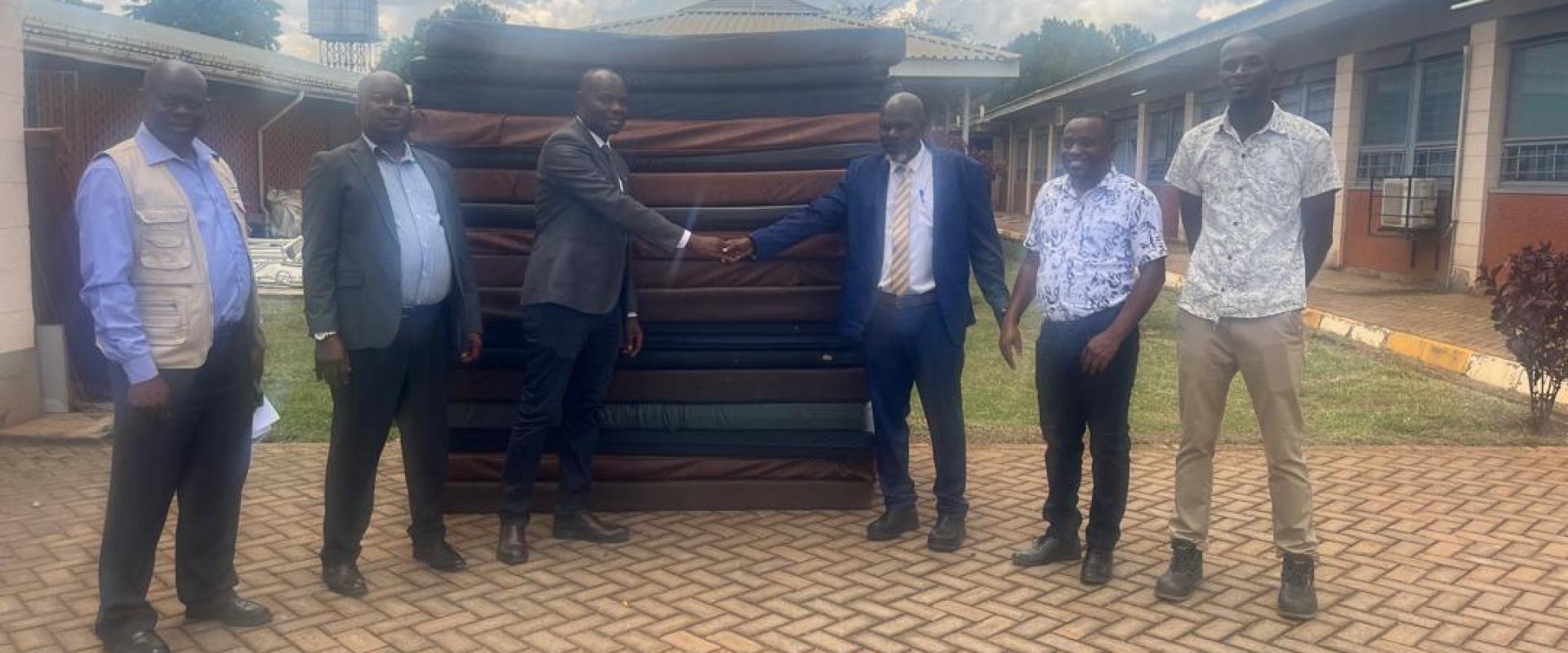 :(center), the Kayunga RRH Board Chairperson Dr. Mpooya Simon handing over 20 mattresses to Hajji Isa Mbooge(yellow neck tie) the Buvuma CAO int the presence of Hajji Salim Kivejinja-Hospital Administrator (2nd left) and Buvuma HCIV Incharge (2nd right)